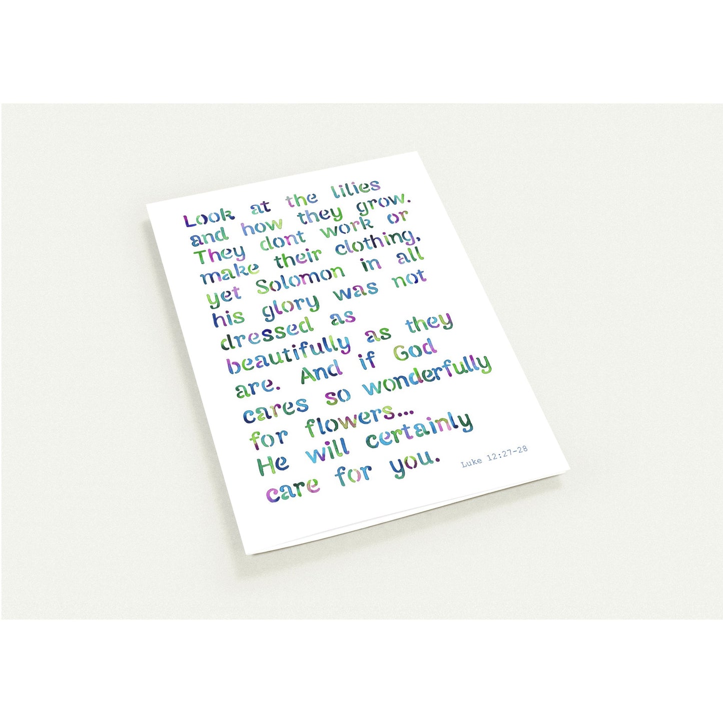A white rectangular art print featuring a Bible verse from Luke 12:27-28 written in a colorful, rainbow-like pixelated font, shown on a light off-white background.