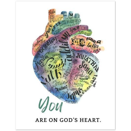 A square wall card featuring a watercolor-style anatomical heart made up of many handwritten names in different colors, with the phrase 'You ARE ON GOD'S HEART.' printed below on a white background.