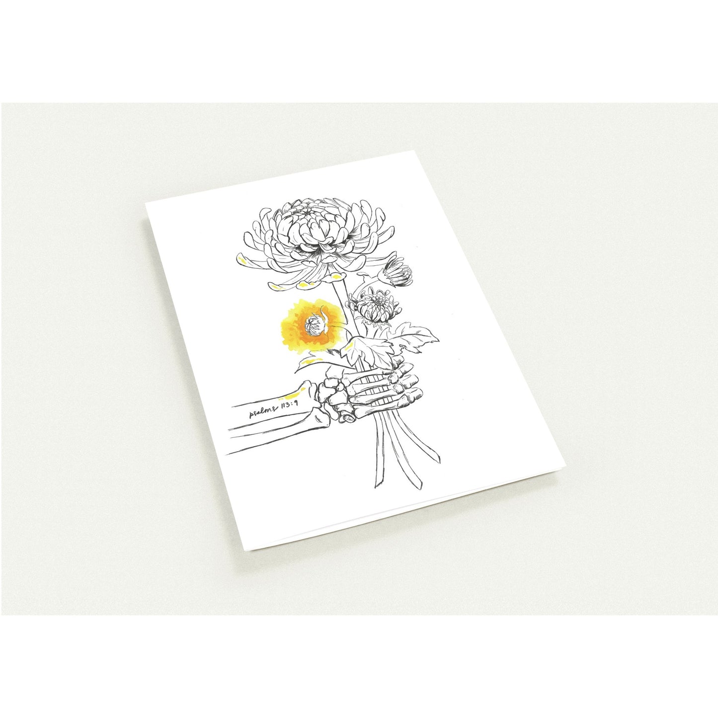 A white art print or card featuring a black line drawing of flowers, including a prominent yellow sunflower, photographed on a light neutral background.