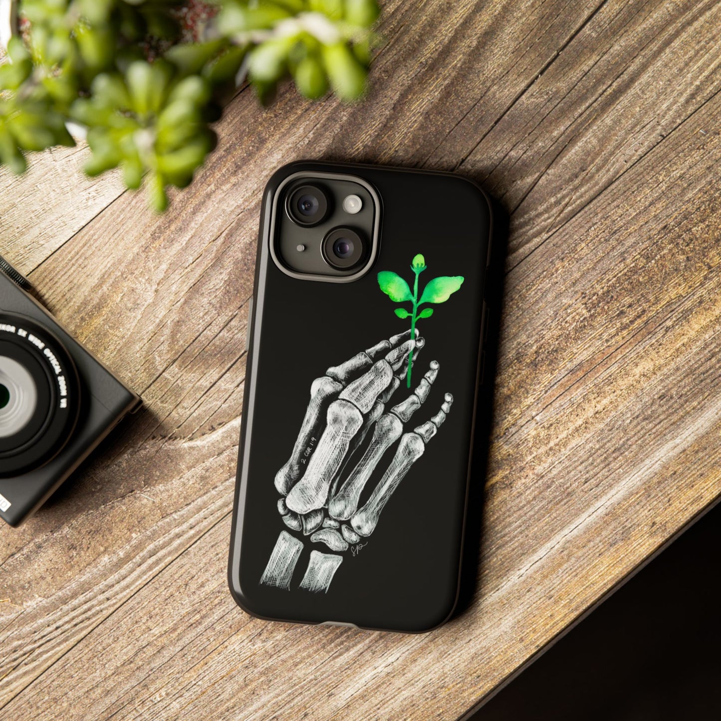 Phone case with skeleton hand holding a plant on a wooden surface