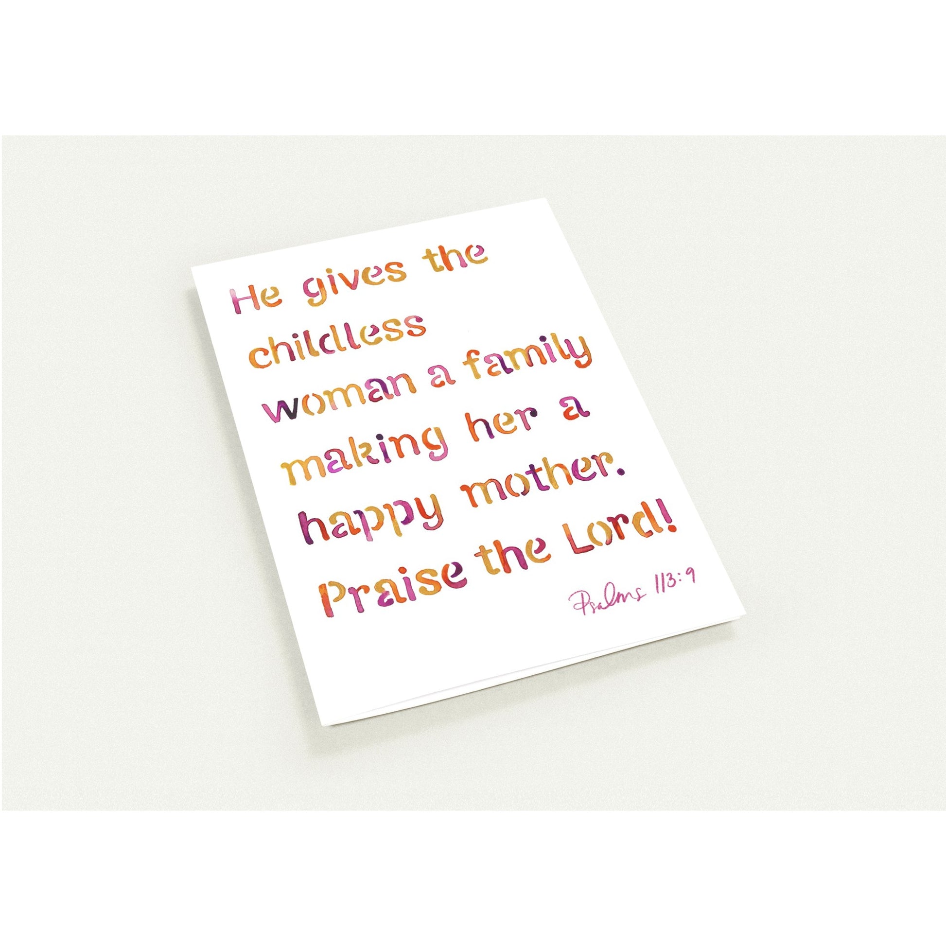 A white greeting card featuring a Bible verse from Psalms 113:9 in a colorful gradient font, photographed at an angle on a light gray background.