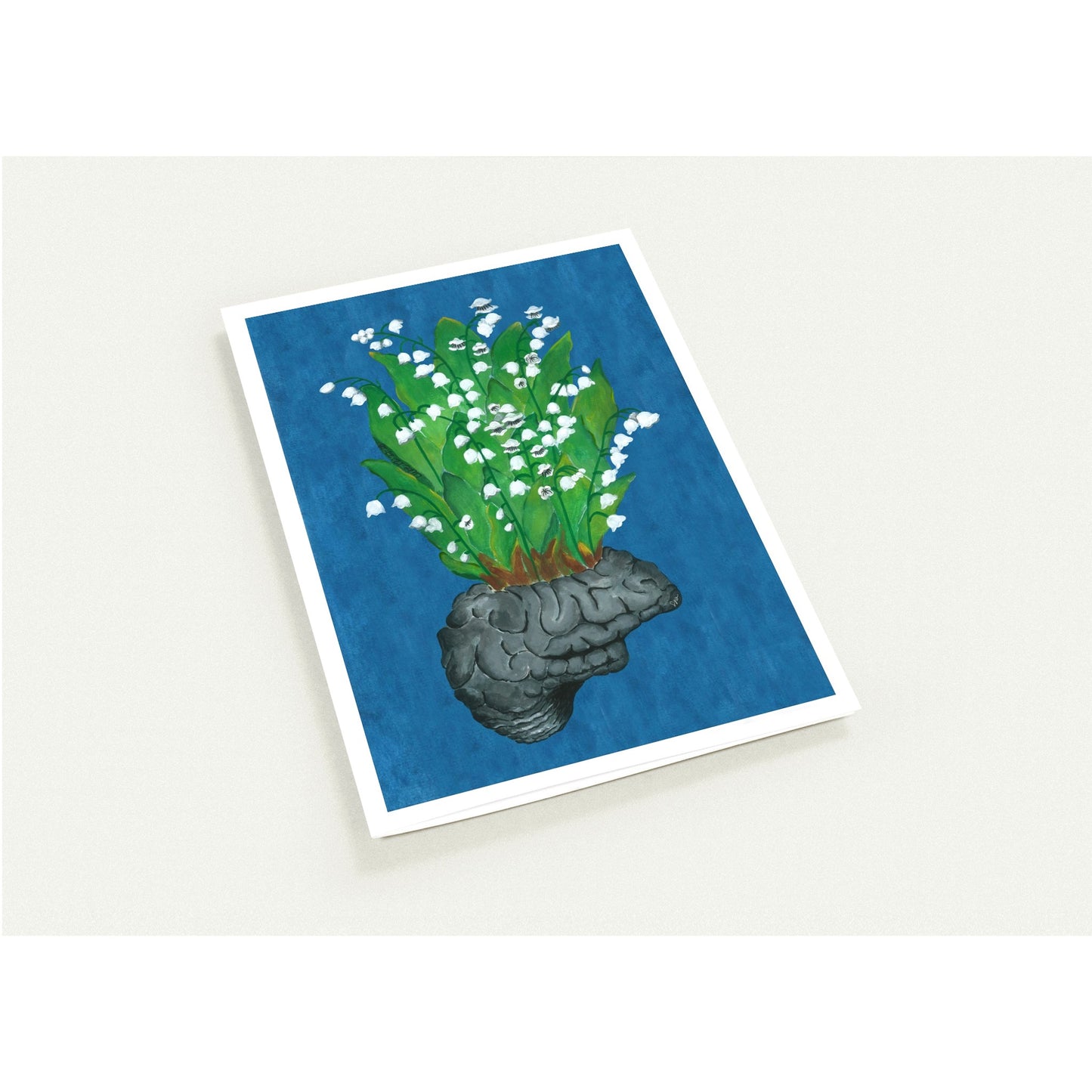 A rectangular card with a white border, featuring a blue background and an illustration of a gray brain-shaped planter holding green stems with small white flowers, photographed on a light neutral surface.