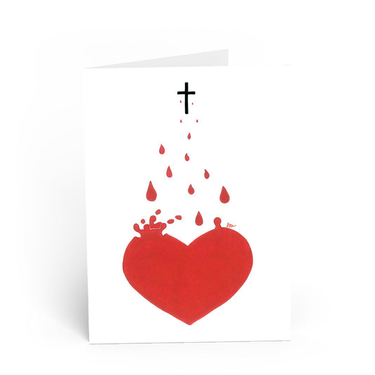 A white greeting card with a minimalist graphic of a red heart, red blood droplets, a small black cross, and splatter details, photographed on a clean white background.