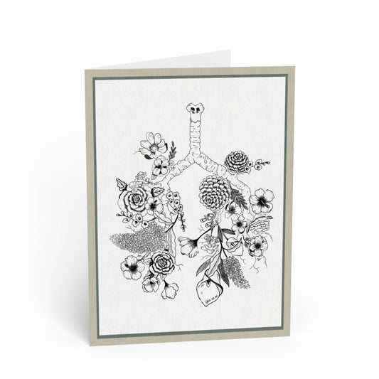A folded greeting card standing upright, featuring a black-and-white botanical illustration of lungs surrounded by flowers and leaves. The card has a light gray border and is photographed on a clean white background.