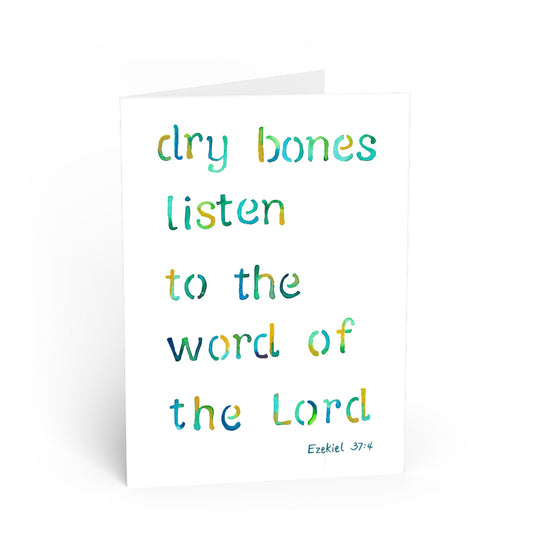 A white greeting card with a watercolor-style quote reading 'dry bones listen to the word of the Lord' in blue and green lettering, with 'Ezekiel 37:4' printed at the bottom right.