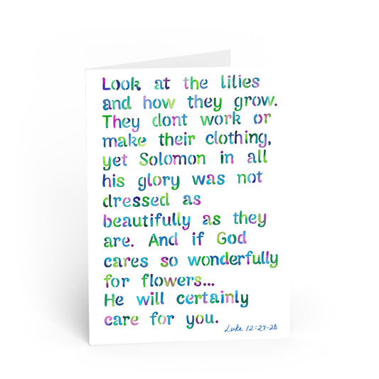 A white greeting card with a colorful, hand-lettered Bible verse from Luke 12:27-28 in pastel rainbow colors, shown on a clean white background.
