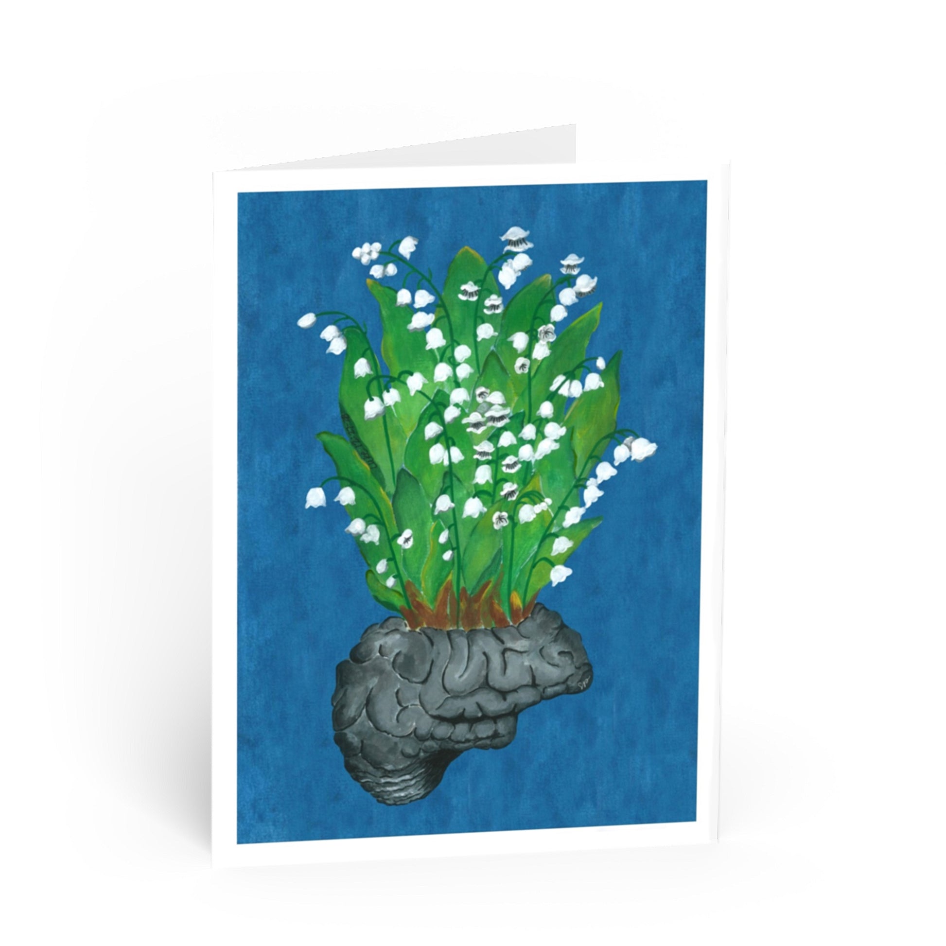 A folded greeting card standing upright on a white background, featuring an illustration of white lily of the valley flowers growing from a gray brain against a textured blue background.