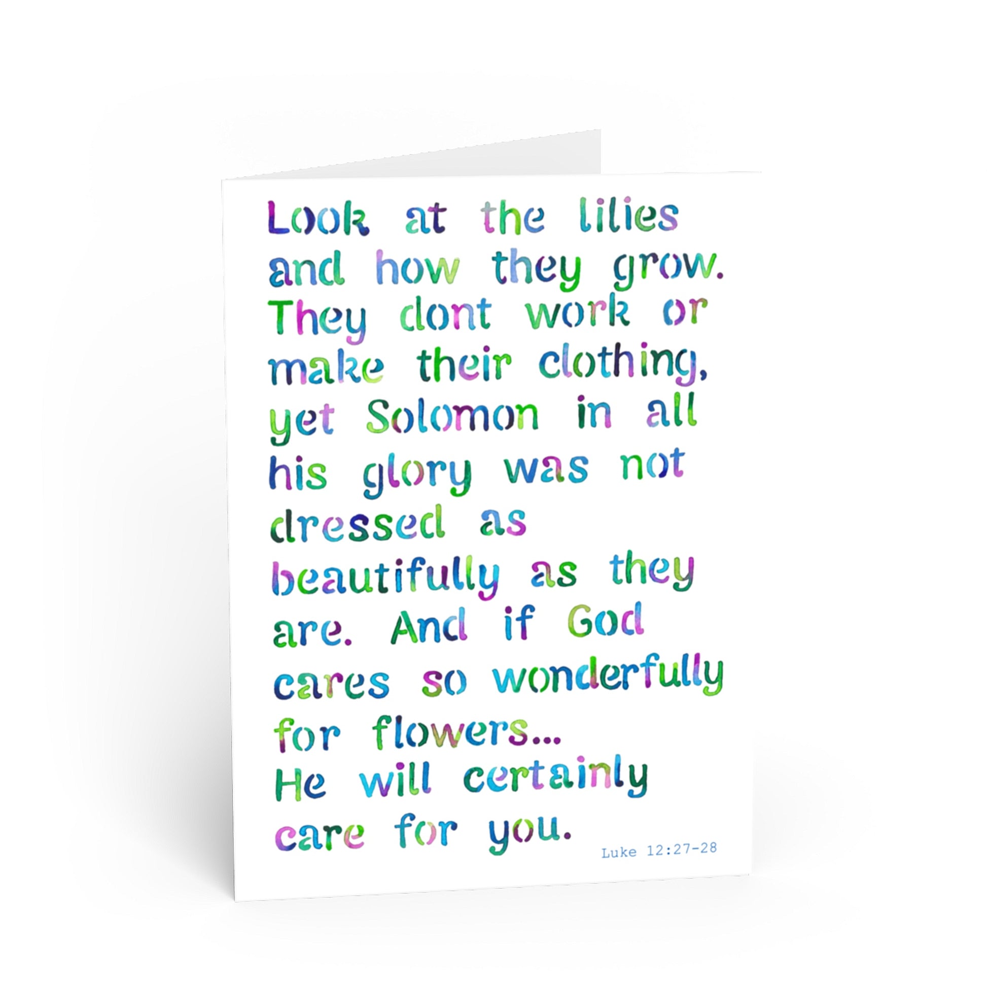 A white greeting card with colorful, hand-lettered text quoting Luke 12:27-28 Solomon and lilies, photographed on a clean white background.