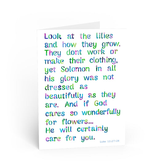 A white greeting card with colorful, hand-lettered text quoting Luke 12:27-28 Solomon and lilies, photographed on a clean white background.