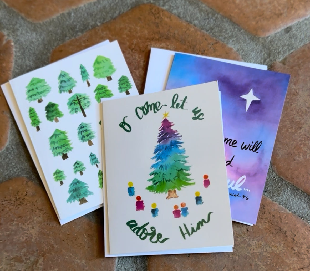 Three greeting cards with different designs on a stone surface that includes envelopes