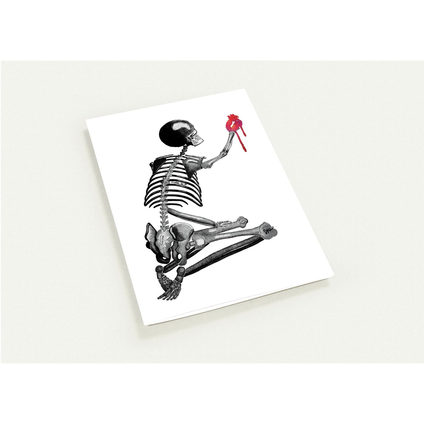 A white rectangular art card shown at an angle on a light neutral background, featuring a black-and-white skeleton illustration holding a small red heart.