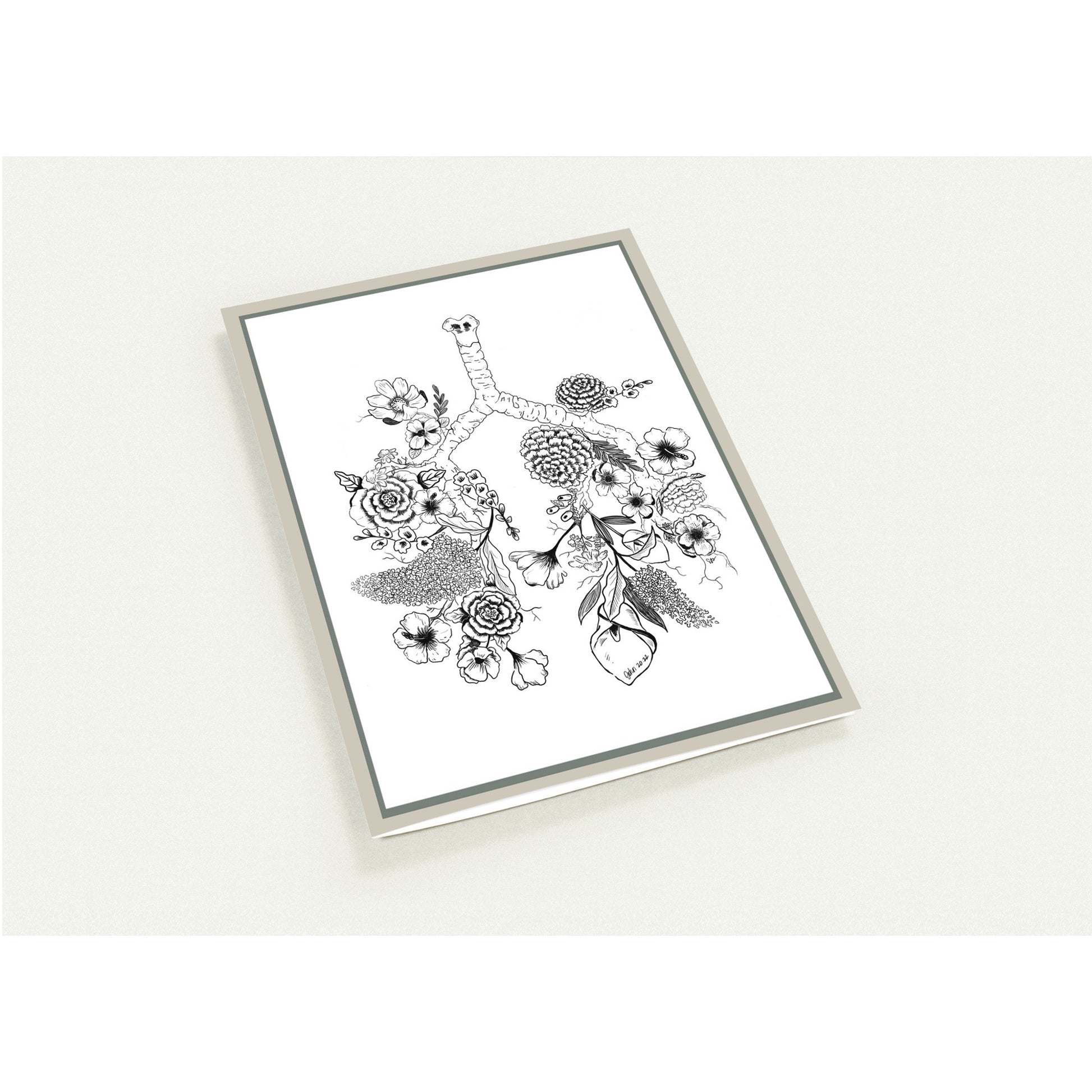 A framed botanical art card featuring black ink illustrations of flowers and leaves on a white background, enclosed in a thin silver frame and photographed against a light neutral backdrop.