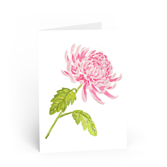 A white greeting card featuring a watercolor-style pink chrysanthemum flower with green leaves, shown standing against a white background.